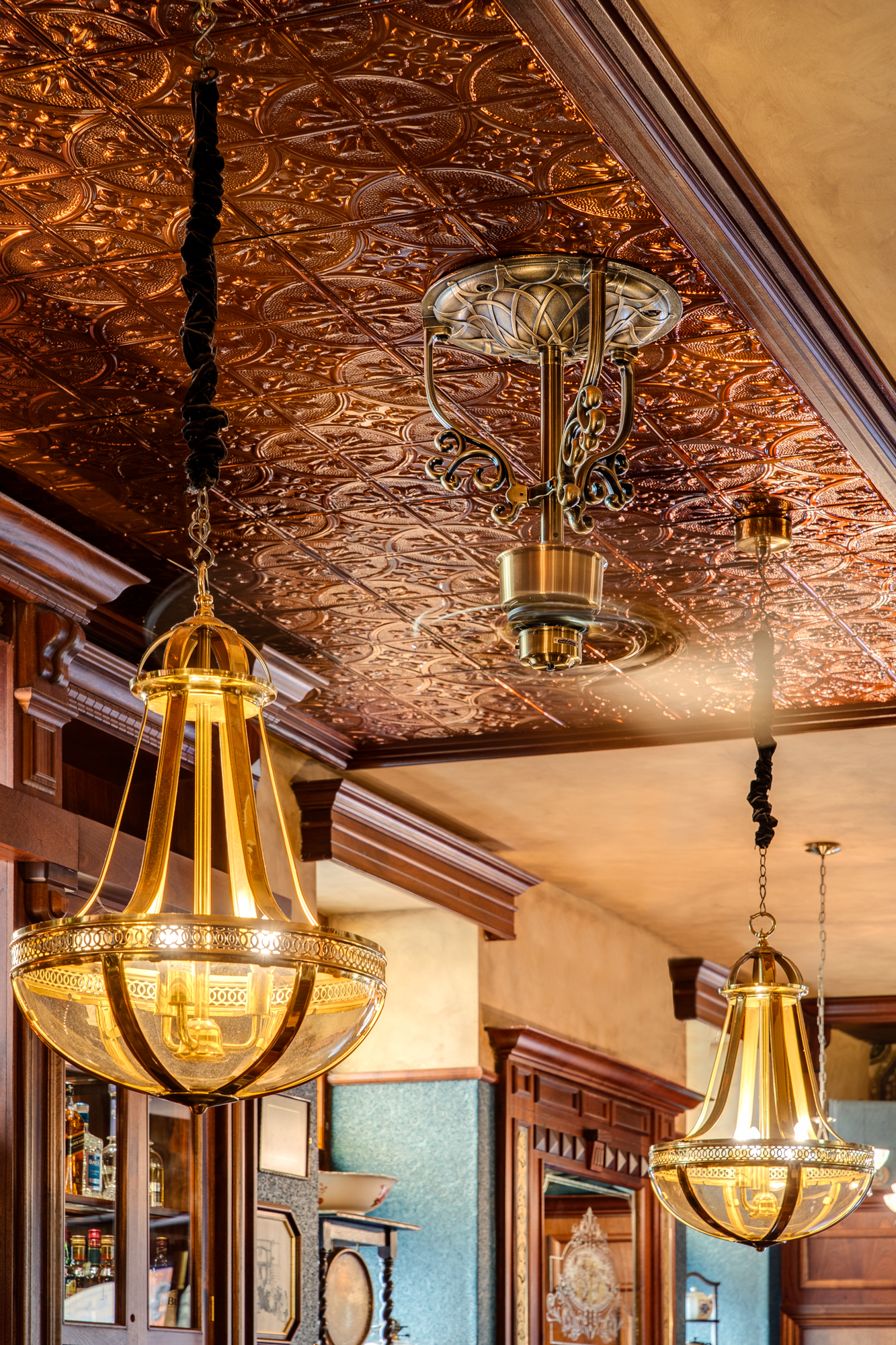 Ornate brass pendant chandeliers hanging from a stamped copper ceiling at The Queen Victoria City Pub