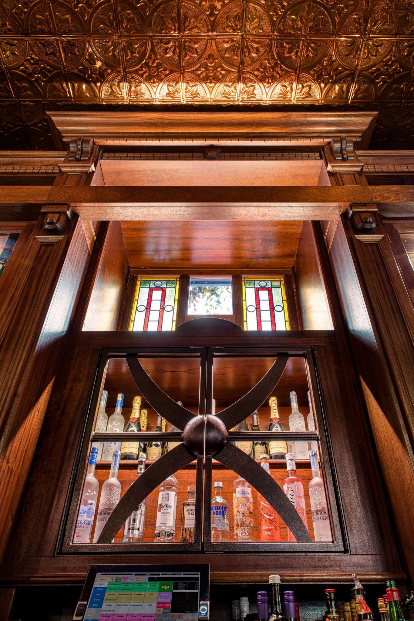 Custom dark wood liquor cabinet with stained glass windows and embossed copper ceiling at The Queen Victoria City Pub